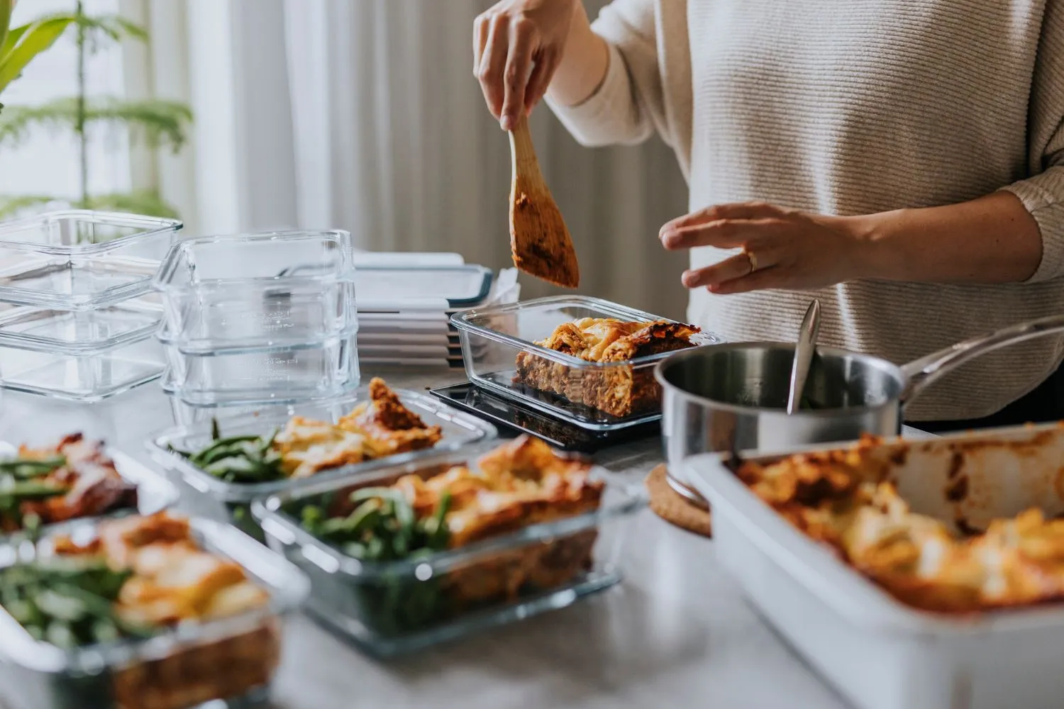 Person in kitchen placing lasagna into storage containers. 